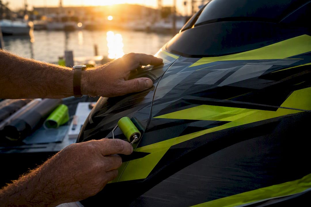 Hands aligning patterned vinyl wrap on jet ski seam