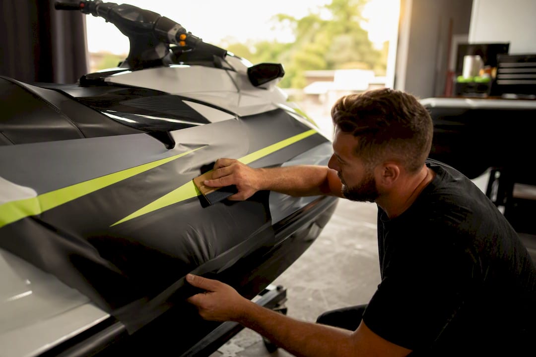 Person smoothing DIY vinyl wrap on jet ski