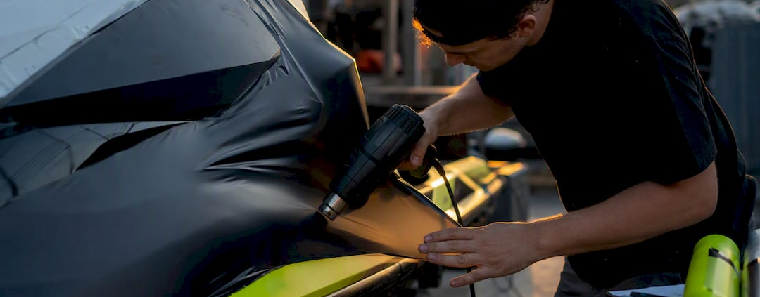 Hands applying vinyl wrap on jet ski hull