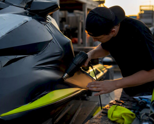 Hands applying vinyl wrap on jet ski hull