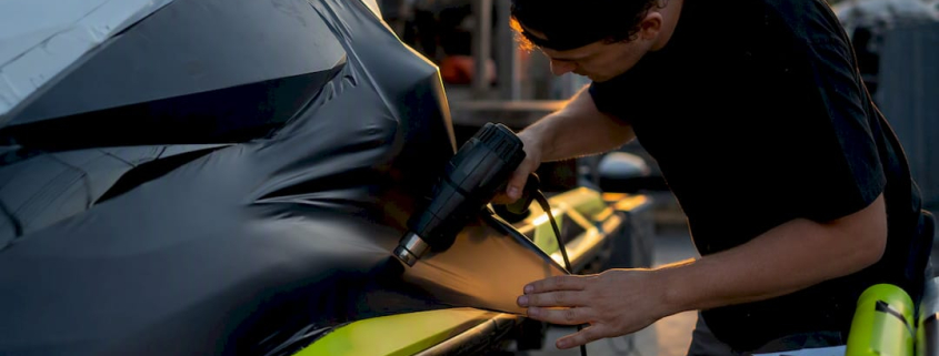 Hands applying vinyl wrap on jet ski hull
